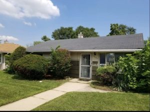 brick fixer upper home in Chicago with overgrown bushes